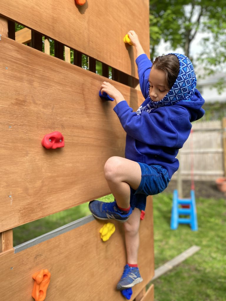 genny scales our diy children's rock climbing wall in the backyard